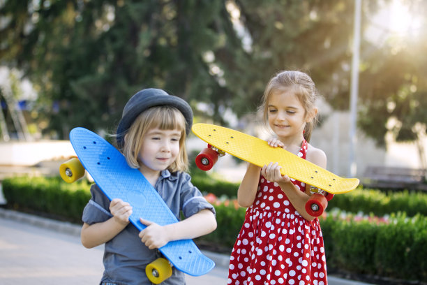 孩子们在公园里玩得很开心。女孩和男孩玩滑板图片下载
