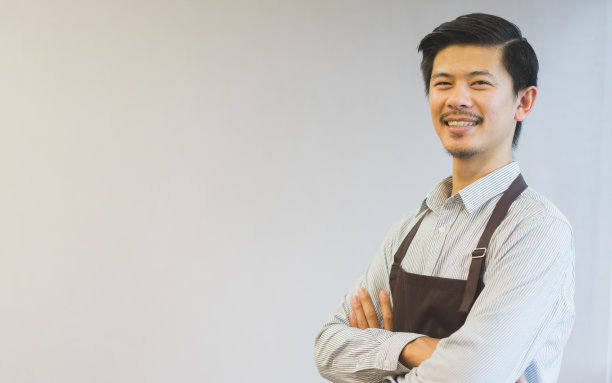近距离观察年轻的亚洲潮男，他穿着正装，系着围裙，交叉着胳膊，站在咖啡馆工作室的背景上(用于复制空间和设计)，千禧一代的生活方式和商业理念图片下载