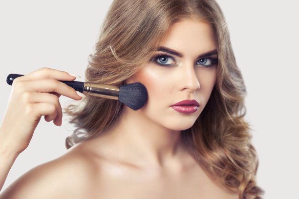 化妆师把粉涂在女孩的脸上，在美容院完成一天的化妆。图片下载