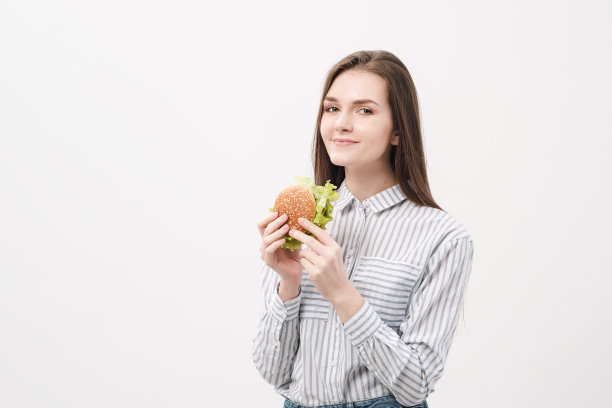 年轻漂亮的黑发女孩站在白底上，手里拿着一个汉堡。图片下载