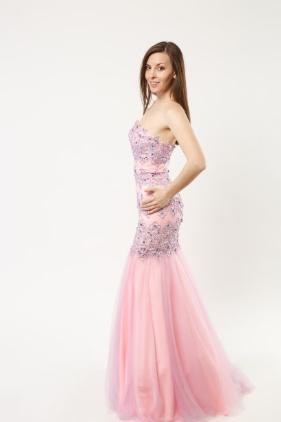 全身照片时装模特女人穿着优雅的晚礼服粉红色礼服摆姿势孤立在白墙背景的工作室肖像。黑发长发的女孩。模拟拷贝空间。侧剖面视图。图片下载