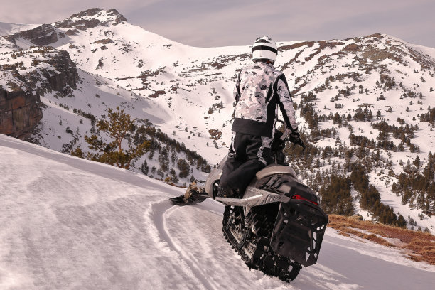 在一个阳光明媚的冬日，一个骑着雪地摩托的人正在寻找一条通往山谷的小路图片下载