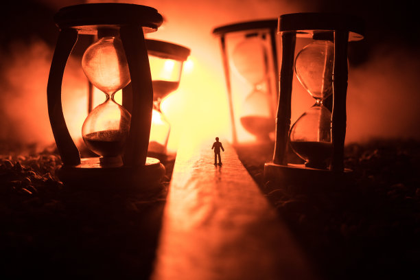 时间的概念。一个男人的剪影站在沙漏中间，在黑暗的背景上有烟雾和灯光。超现实主义的装修图片图片下载