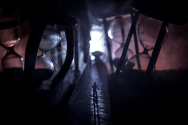 时间的概念。一个男人的剪影站在沙漏中间，在黑暗的背景上有烟雾和灯光。超现实主义的装修图片图片下载