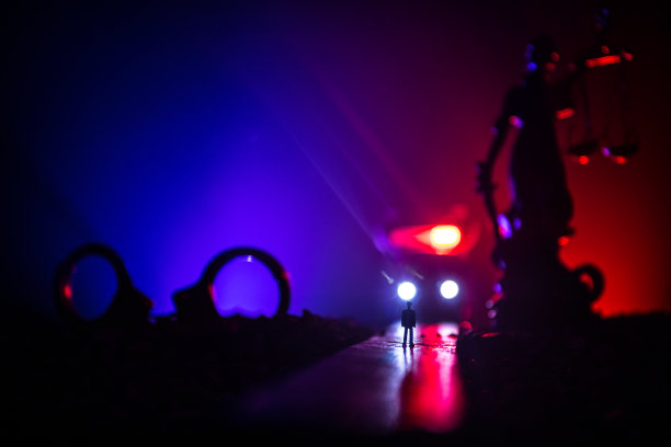 合法的法律概念。手铐的剪影与正义的雕像在背后与闪烁的红色和蓝色的警察灯在雾蒙蒙的背景。有选择性的重点图片下载