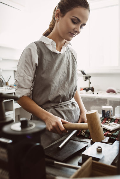 自信的运动。女性珠宝商用锤子制作银戒指的垂直照片图片下载