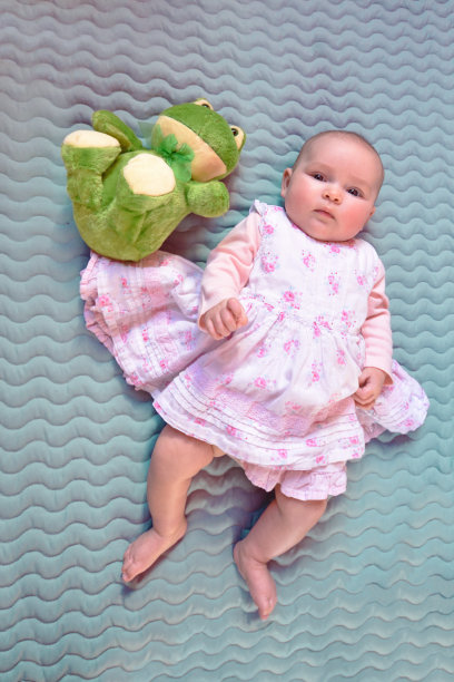 小女孩在粉红色的裙子躺在绿色的青蛙填充玩具旁边图片下载