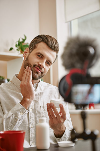 柔软的皮肤。垂直照片积极的男性美容博主在他的脸上涂抹化妆品，而直播。图片下载