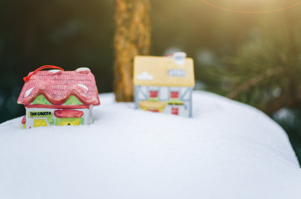 原来的陶瓷玩具房子站在圣诞松树树枝上的雪。冰冻森林装饰的自然照片。节日快乐装饰明信片。图片下载