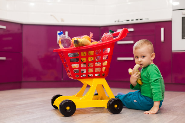 小男孩吃香蕉。快乐的小男孩推着购物车。穿着休闲装的小孩推着儿童塑料购物车。图片下载