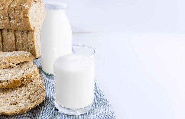 一瓶牛奶和一杯牛奶与切片面包布在室内的背景食品和健康的概念。与复制空间的文本。图片下载