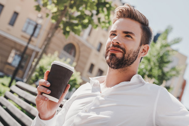 放松的时间。一个年轻人坐在公园里，一边喝咖啡，一边看向别处图片下载