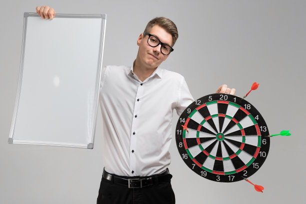 年轻男子戴眼镜与目标与飞镖不在中心和空盘子在他的手孤立在白色背景图片下载