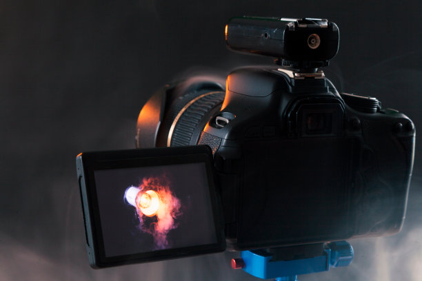 蓝色三脚架上的相机照片，在摄影棚里拍摄烟雾中的专业照明设备。工作室灯光和烟雾设备。带无线电同步器的相机图片下载