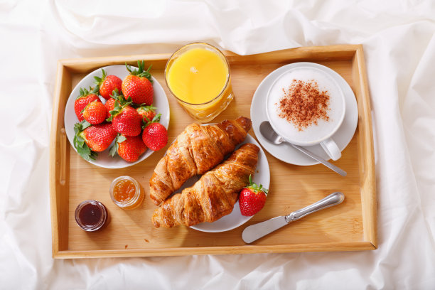 早餐托盘放在床上:一杯卡布奇诺、橙汁、羊角面包和新鲜草莓图片下载