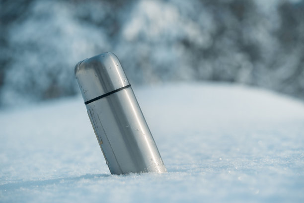 雪中装有咖啡或茶的金属热水瓶。图片下载