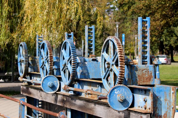 未使用的小水坝齿轮生锈的齿轮排成一排，破旧的油漆用坚固的螺栓安装在金属梁上图片下载