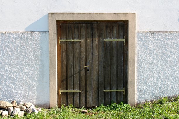 地下室的木制入口门有破旧的木板和坚固的金属铰链安装在混凝土墙上，前面是未修剪的草和岩石图片下载