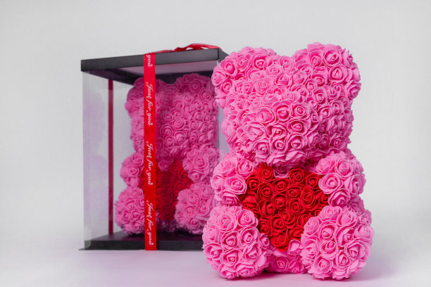 粉红色的泡沫玫瑰泰迪熊玩具。同样的泰迪在清楚的盒子与黑色纸封面上的背景。泰迪熊掌里的红心。股票照片孤立的白色背景。图片下载