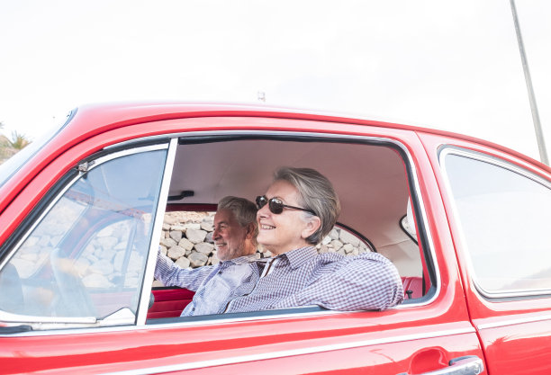 漂亮的成年老年白人夫妇有乐趣和爱在一辆红色的老旧的车停在路上。微笑，一起享受旅行。给好人的幸福和生活方式。暑假旅行图片下载