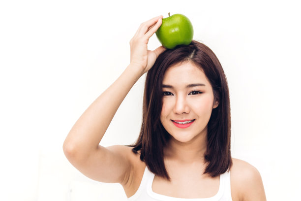 一个女人在白色的背景上拿着并吃着新鲜的绿苹果。节食的概念。健康的生活方式图片下载