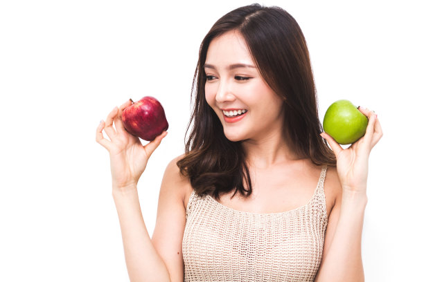 一个女人在白色的背景上拿着并吃着新鲜的绿苹果。节食的概念。健康的生活方式图片下载