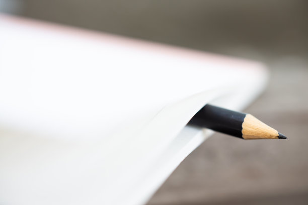 一个黑色的铅笔夹在白色笔记本之间的木头背景，近距离微距拍摄，选择性聚焦，文具的概念图片下载