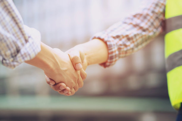 一名工程男手持文件计划的近距离拍摄施工项目工人与两名商人握手，代表好项目成功批准，祝贺。户外建筑。图片下载