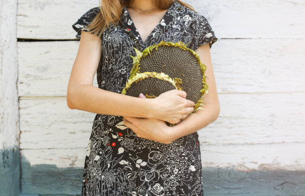 一个带着旧皮箱的时髦女孩站在木墙旁边。时尚的旅游照片。村子里穿着黑衣服的女人。复古乡村的概念。图片下载