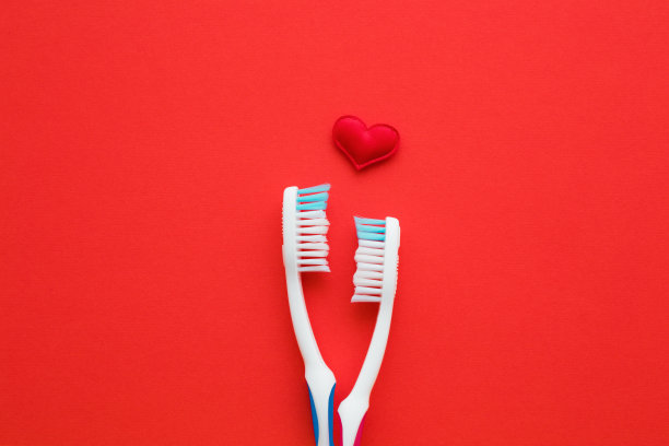 红色背景上有两个心形的白色牙刷。男女牙齿卫生。住在一起。爱的概念。空的地方，可爱的文字，引用或语录。平的。关闭了。图片下载