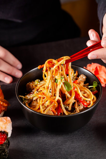 亚洲美食的概念。在一家餐馆里，女孩手里拿着日本筷子，吃着黑色盘子里的中国面条。的背景图片。本空间图片下载