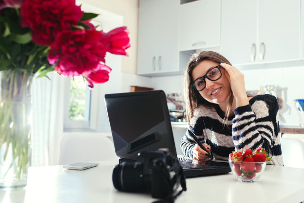 自由摄影师在家工作。女性使用相机和平板电脑在笔记本电脑上工作。启动图片下载