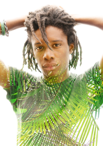 一张深色皮肤、梳着脏辫、双手放在脑后的男子的双重曝光照片，加上一张郁郁葱葱的绿色热带植物的照片图片下载