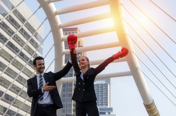 在现代城市中，英俊的商人用拳击手套举起他的女商业伙伴的手，庆祝，胜利者的姿态，团队领导，成功，支持，团队合作，社区，自信的概念图片下载