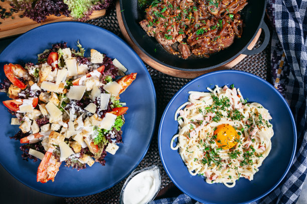 俯视图上提供的食物表。凯撒虾仁沙拉，肉盘，烤干酪沙司在蓝色的盘子。餐厅菜单，食谱照片与复制空间。美味的扁平食物。图片下载