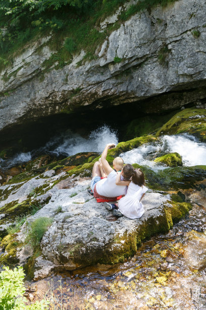 母亲和孩子们在自拍，坐在山溪旁的岩石上的家庭旅行。图片下载