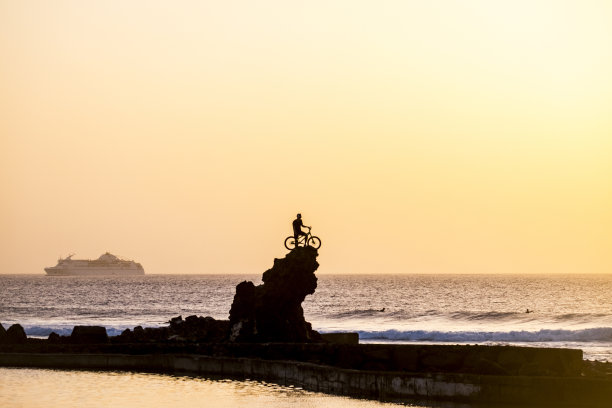 运动员与山地车越过一个大悬崖的成功概念与海洋和游客的背景游轮。日落和运动自行车活动概念-海浪和冲浪与自行车户外极限图片下载