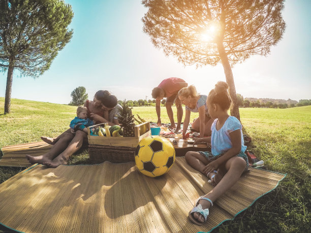 快乐的家庭准备在公园户外野餐-年轻的父母与孩子在夏季时间的乐趣-食物，周末的生活方式和友谊的概念-集中左人们的头图片下载