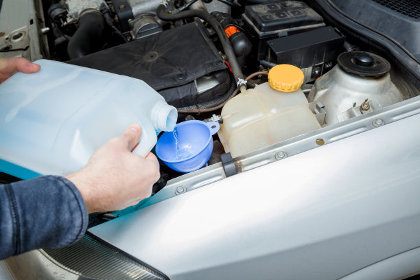 人工从车库挡风玻璃的塑料瓶中通过漏斗将蓝色清洗液注入汽车油箱。关心的是汽车。图片下载
