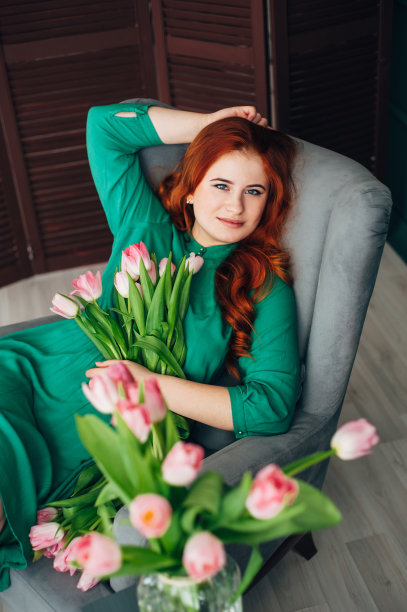 一个漂亮的红头发女人拿着一大束郁金香坐在椅子上。图片下载