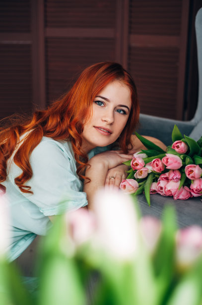 一个漂亮的红头发女人拿着一大束郁金香坐在椅子上。图片下载