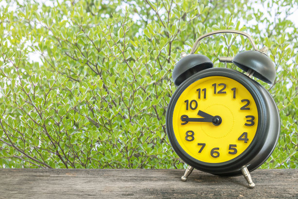 特写闹钟为装饰显示时间在十点四十五分或早上9:45在旧木桌上的绿色树叶在公园纹理的背景图片下载