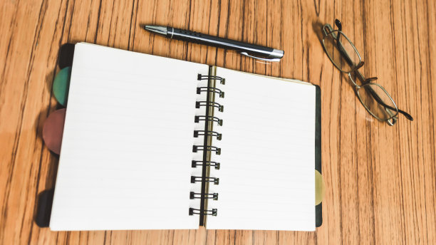 书桌上有打开的笔记本和空白页，眼镜和一支笔。商业静物生活概念与办公用品桌上。教育、工作和规划理念。图片下载