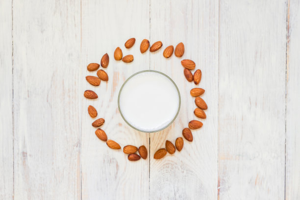 俯视图自制杏仁牛奶在一个玻璃杯和散落的坚果在木制背景。健美的。副本的空间。图片下载