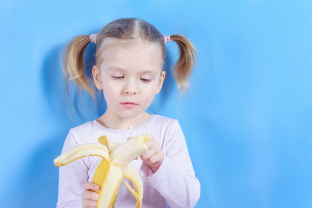 一个金发小女孩正拿着一个香蕉。这孩子清洗水果的果皮。明亮的照片与文本空间，复制空间。图片下载