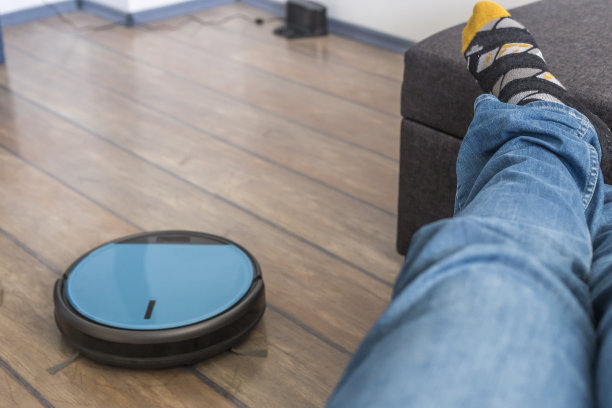 一个人在沙发上休息，而机器人真空吸尘器正在工作图片下载