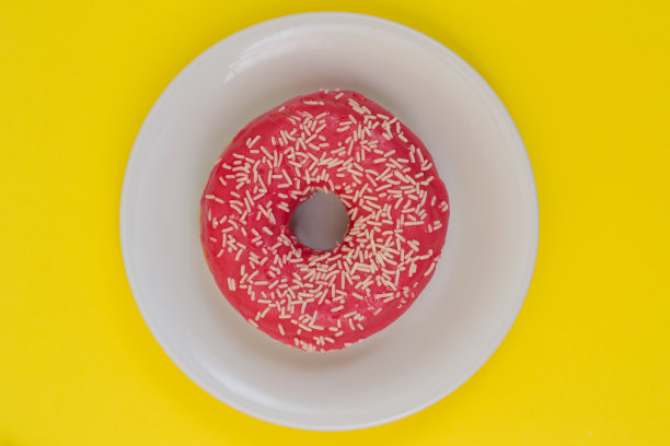 近距离的照片美味的釉面奶油在里面的甜甜圈盘孤立在黄色的背景。俯视图，简约风格图片下载