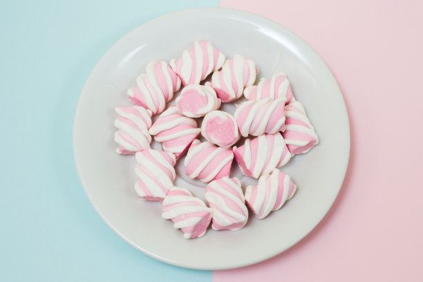 俯视图照片的盘子充满美味的棉花糖在中间一半蓝色一半粉红色的背景。简约风格，柔和的色彩，特写照片图片下载