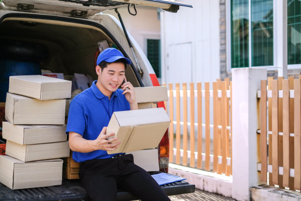 穿着蓝色制服的年轻送货员打电话给客户送货。图片下载