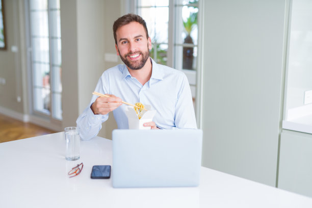 商人吃带走的亚洲面条食品，同时工作用电脑笔记本电脑和微笑图片下载
